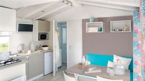 A compact kitchen with a gas stove, microwave, and a small dining area with a table and chairs. - Camping Saint Paul (Lyons-la-Foret)