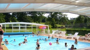 An indoor swimming pool with a covered roof, surrounded by lounge chairs and a grassy area. - Camping Saint Paul (Lyons-la-Foret)