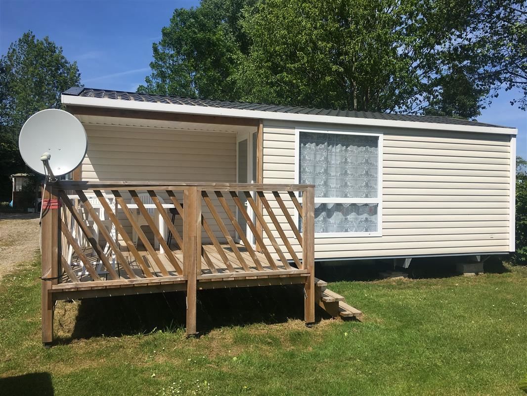 Une maison mobile équipée d’une antenne parabolique, d’une terrasse en bois et d’une fenêtre.