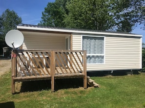 A mobile home with a satellite dish, a wooden deck, and a window. - Camping Saint Paul (Lyons-la-Foret)