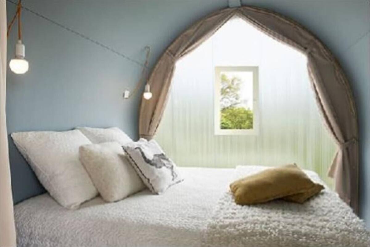 Un dormitorio con cama, almohadas y una ventana con cortinas.