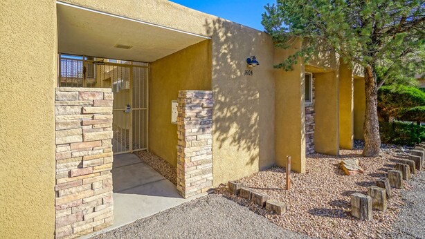 A building with a stone facade, a gated entrance, and a tree in the background. - ABQ Uptown Condo near I-40, 2bd/1ba, AC! (Albuquerque)
