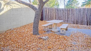 A backyard with a tree, a wooden fence, and a stone bench. - ABQ Uptown Condo near I-40, 2bd/1ba, AC! (Albuquerque)