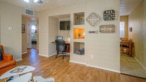 A spacious living room with hardwood floors, a ceiling fan, a TV, and a dining area with a table and chairs. - ABQ Uptown Condo near I-40, 2bd/1ba, AC! (Albuquerque)
