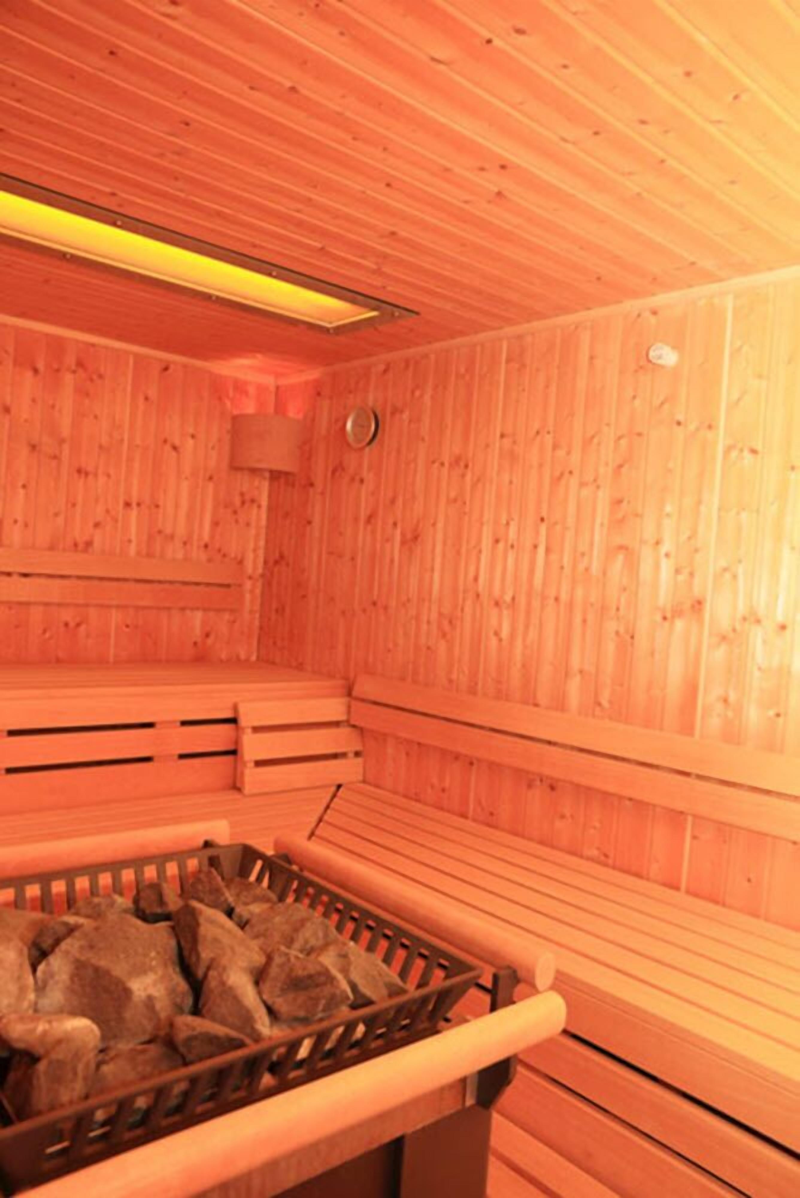 A sauna with wooden walls and benches, a bench with a basket of stones, and a visible light fixture.