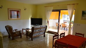 Uma sala de estar com sofá, cadeiras, televisão e mesa de jantar com cadeiras.