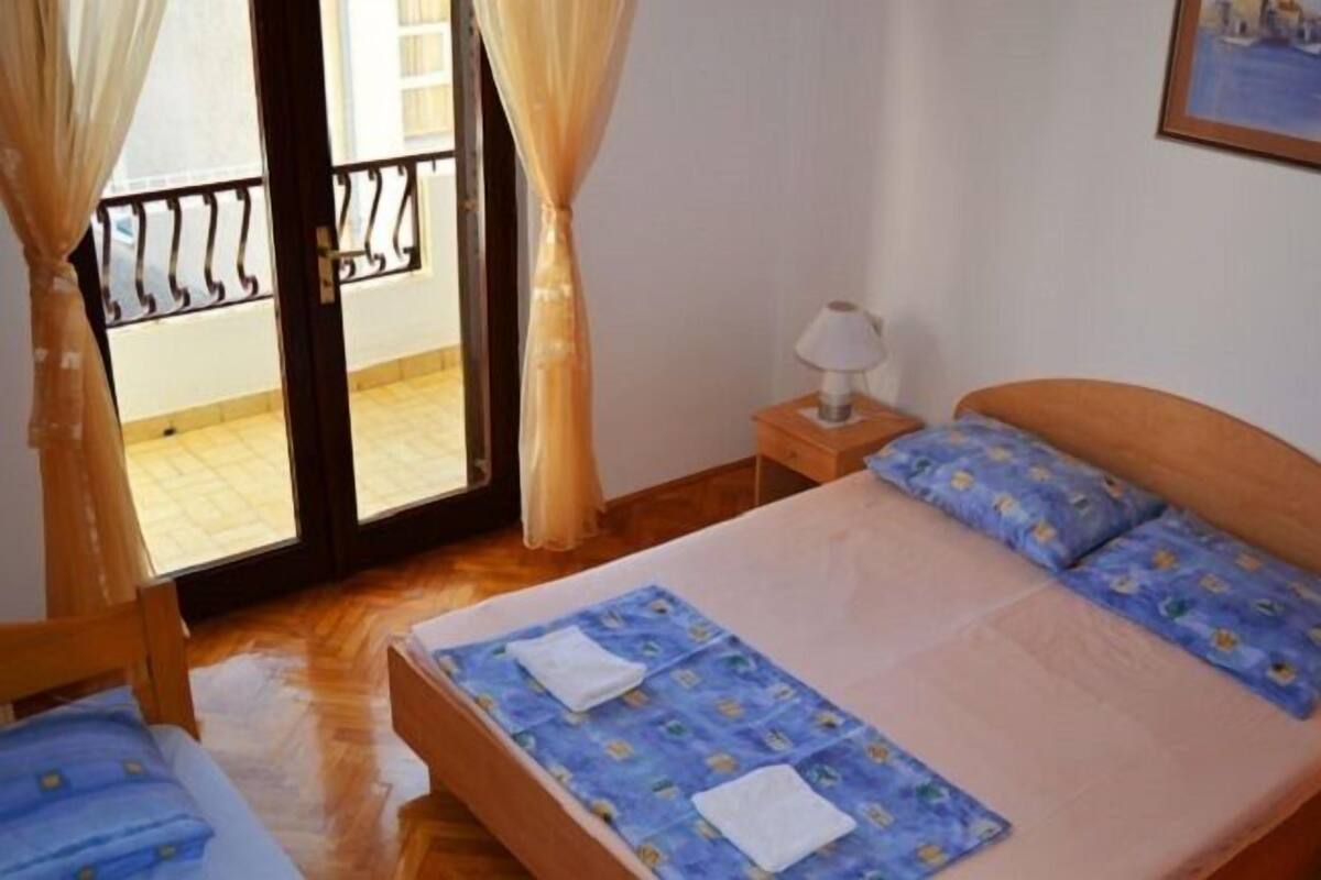 A bedroom with a bed, a nightstand, a window with curtains, and a view of the outside balcony.