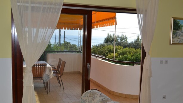 Uma varanda com mesa e cadeiras, vista para o mar e um quadro na parede.