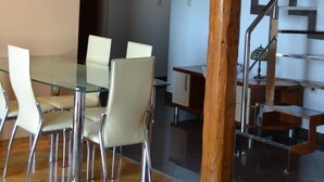 Um interior moderno com mesa de jantar de vidro, cadeiras brancas, escada de madeira e uma cruz na parede.
