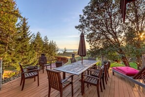 A wooden deck with a table and chairs, surrounded by trees and a view of the ocean. - Gramma's 4BR Home, Lake, Wooded, Hot Tub, Swim, Swings, Gated Estate, Gorgeous (Friday Harbor)