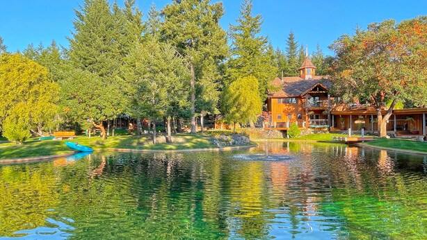 A lakeside property with a large house, a pond, and surrounding trees. - Gramma's 4BR Home, Lake, Wooded, Hot Tub, Swim, Swings, Gated Estate, Gorgeous (Friday Harbor)