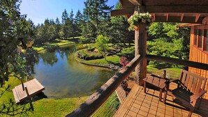 A wooden deck with a view of a pond and surrounding greenery. - Gramma's 4BR Home, Lake, Wooded, Hot Tub, Swim, Swings, Gated Estate, Gorgeous (Friday Harbor)