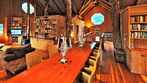 A wooden interior with a long dining table, bookshelves, a fireplace, and a television. - Gramma's 4BR Home, Lake, Wooded, Hot Tub, Swim, Swings, Gated Estate, Gorgeous (Friday Harbor)