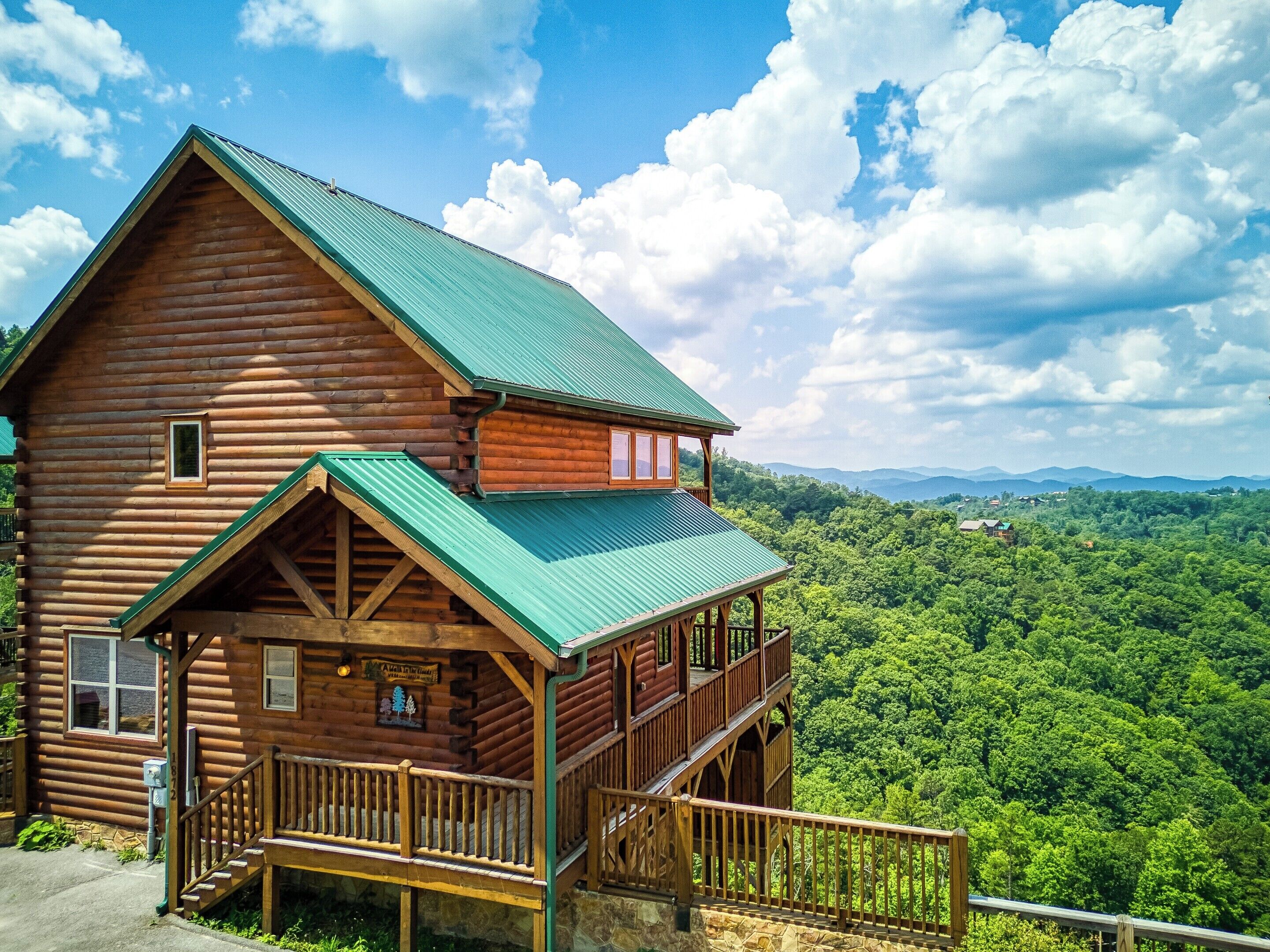 A log cabin with a green metal roof, a balcony, and a scenic view of a forested mountain range.