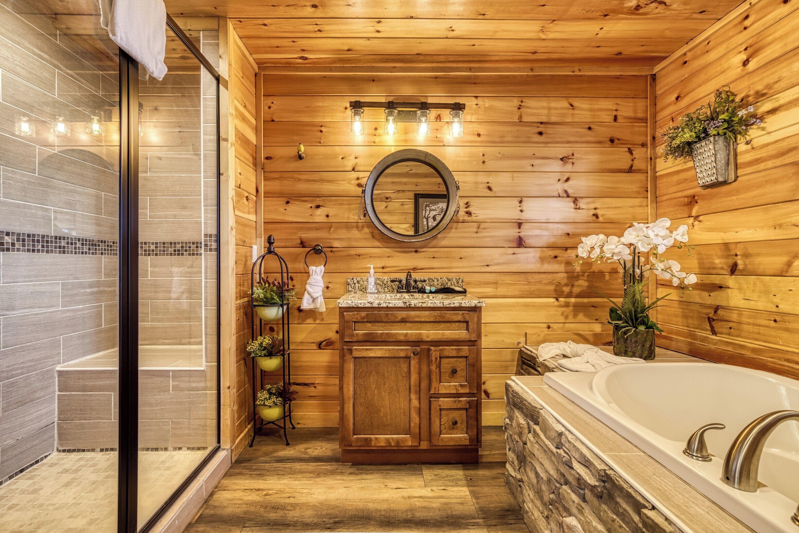 Un baño de cabaña de madera con un lavabo de piedra, un espejo grande y una bañera.