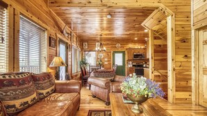 Ein gemütliches Blockhaus-Interieur mit einer Ledersofa, einem Esstisch mit Blumenvase und Holzwänden.