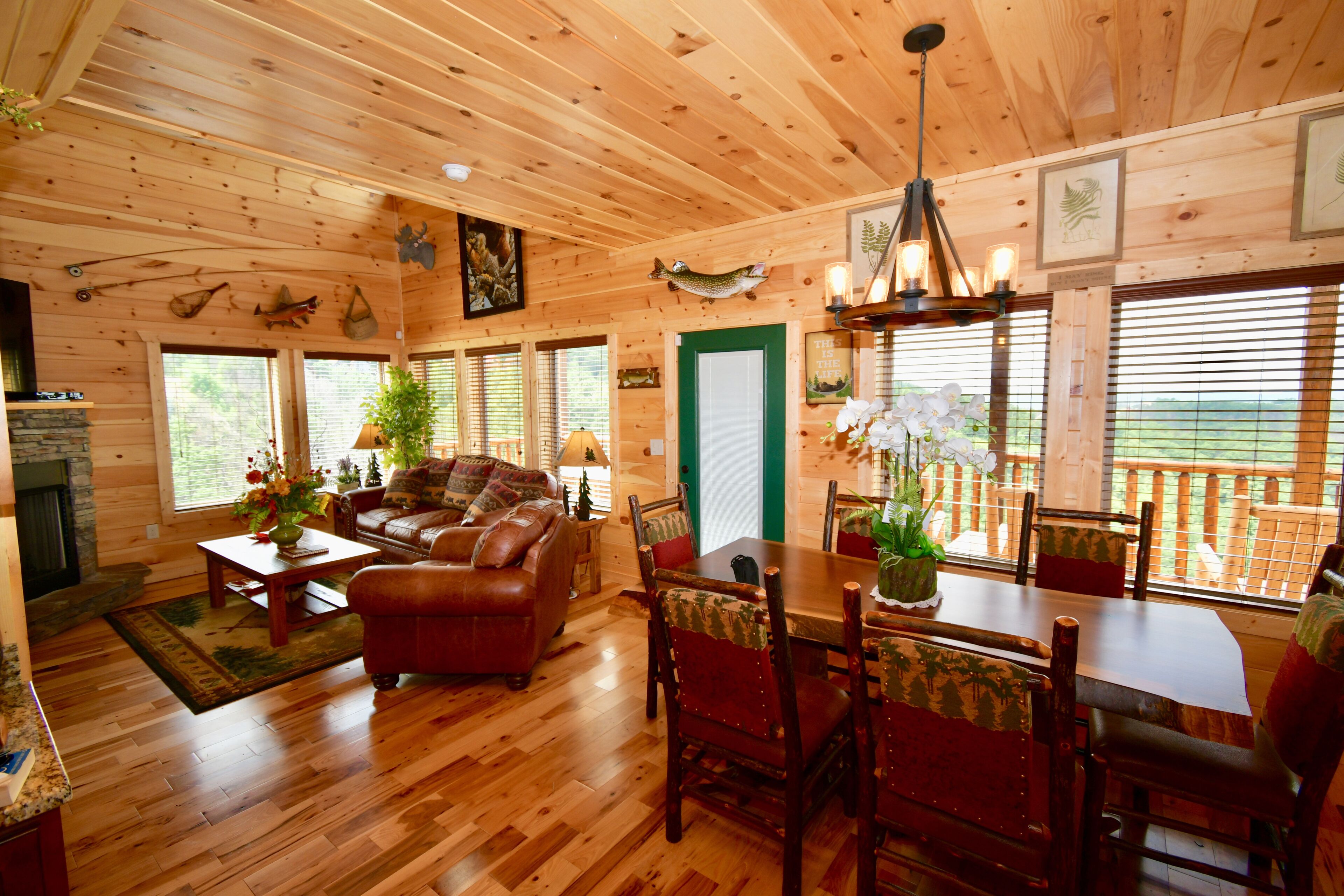 A cozy cabin interior with a wooden floor, a leather sofa, a dining table with chairs, and a fireplace.