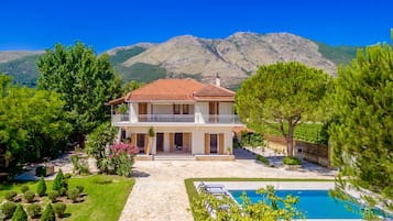 A two-story house with a balcony, surrounded by a well-maintained garden and a swimming pool.