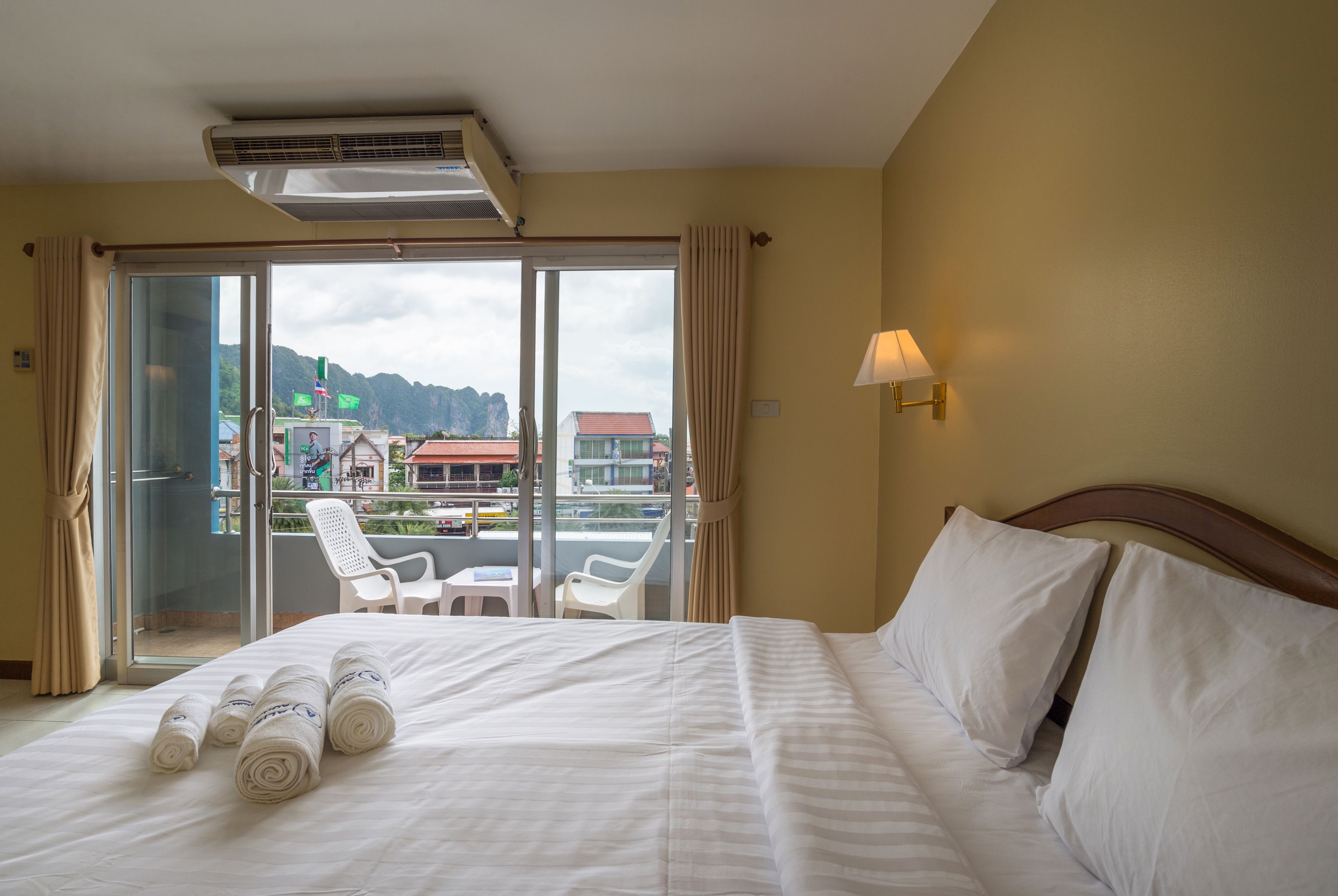 A hotel room with a bed, a balcony with chairs, and a view of buildings and mountains.