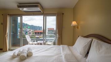 A hotel room with a bed, a balcony with chairs, and a view of buildings and mountains.