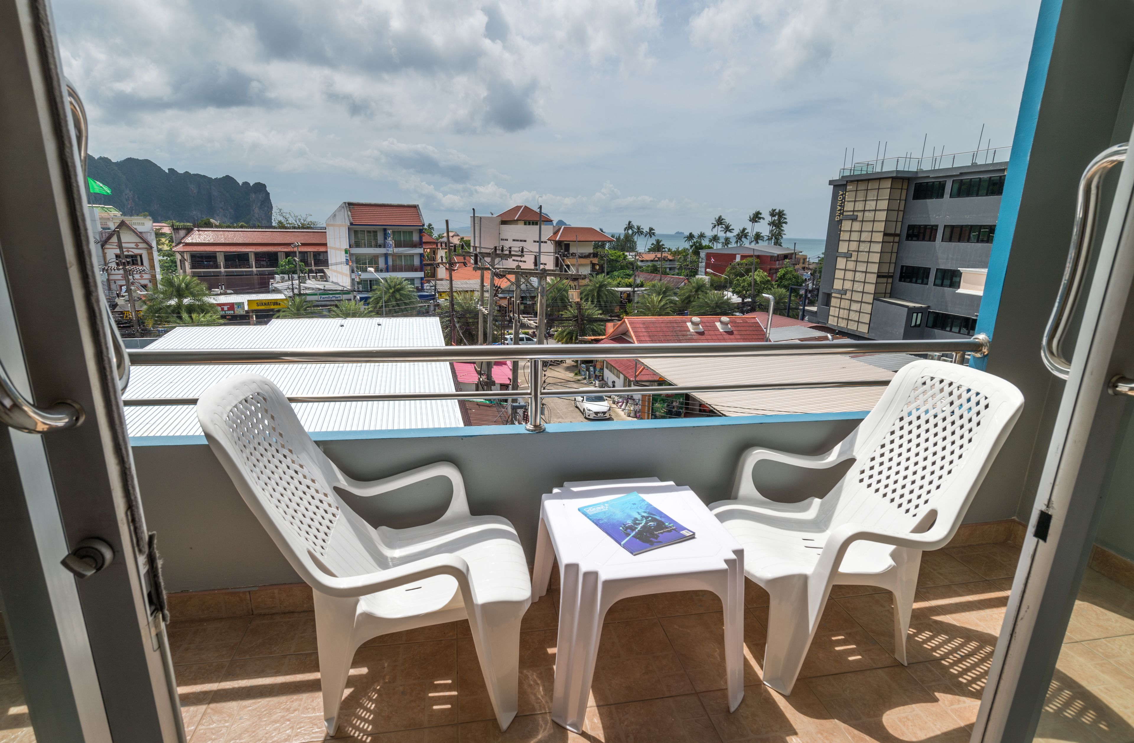 A balcony with two white plastic chairs and a small table, overlooking a cityscape with buildings and palm trees.