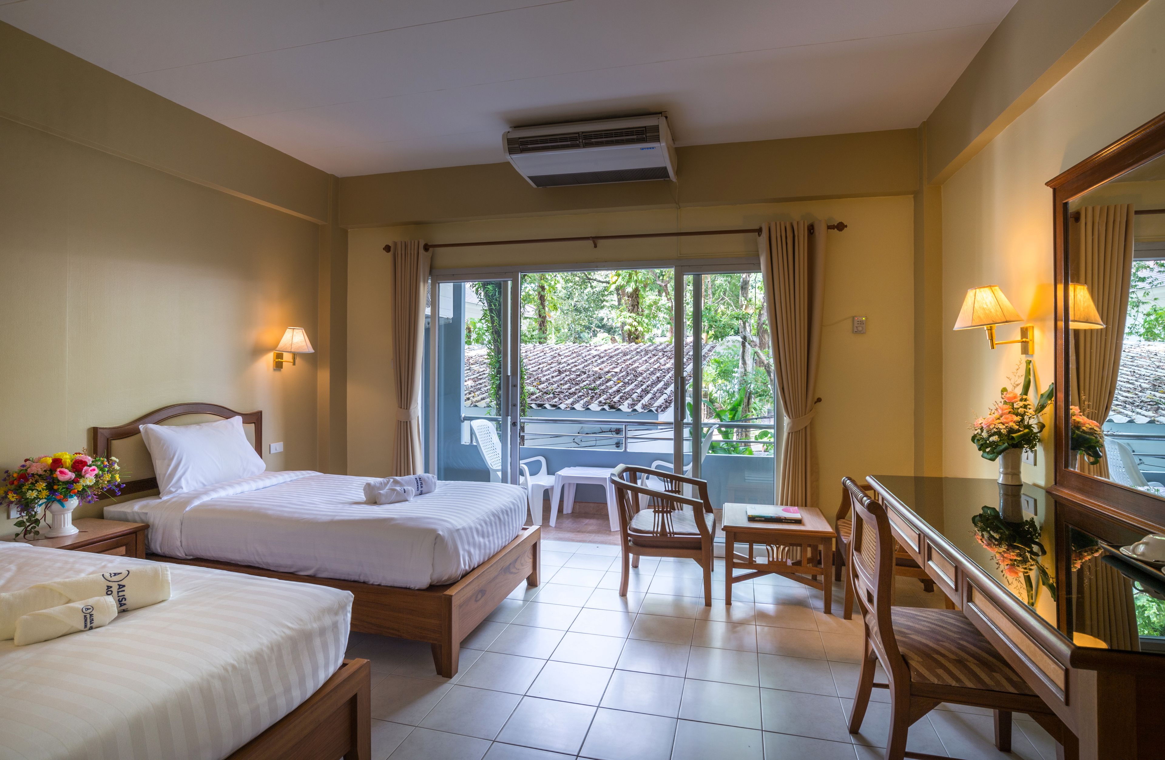 Habitación de hotel con dos camas, un escritorio, sillas y un balcón con vistas a zonas verdes.