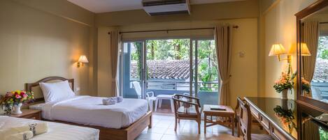 Habitación de hotel con dos camas, un escritorio, sillas y un balcón con vistas a zonas verdes.
