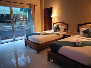 Habitación de hotel con dos camas, una puerta corrediza de vidrio al exterior y una mesita de noche con lámpara.