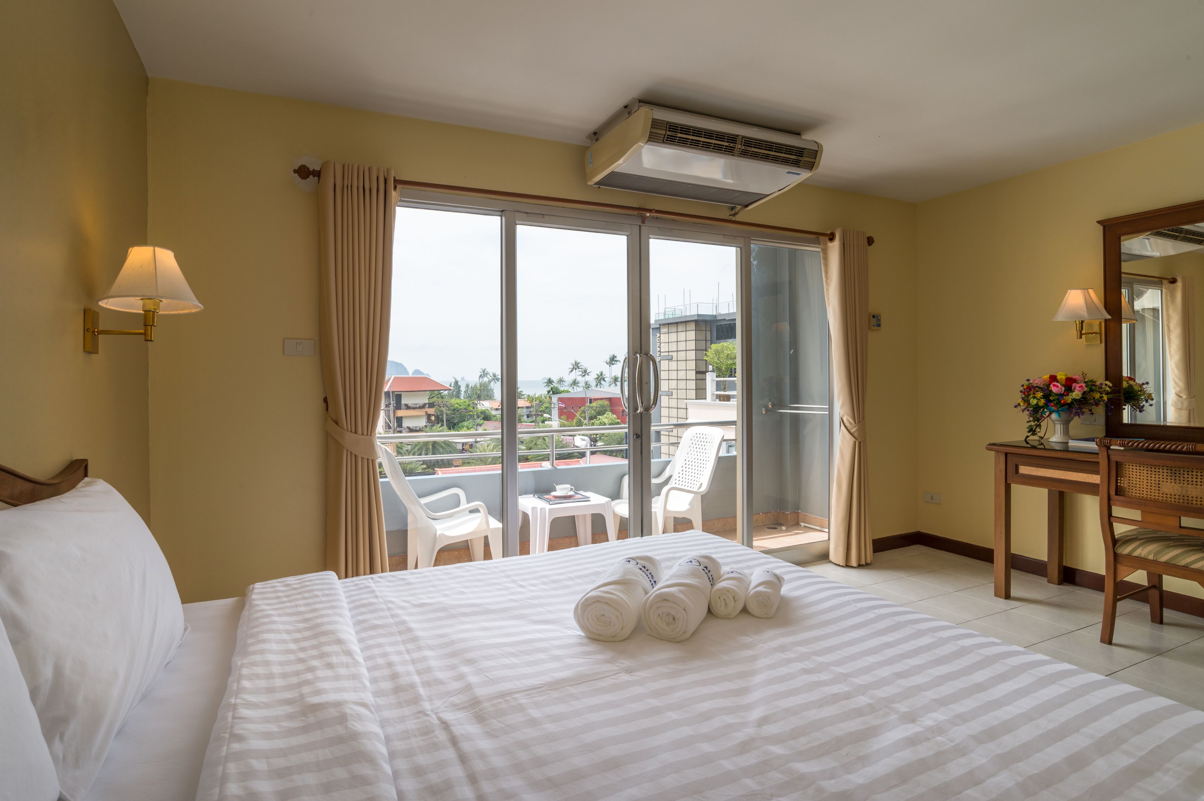 Una habitación de hotel con cama, un balcón con sillas, una mesa y un espejo.