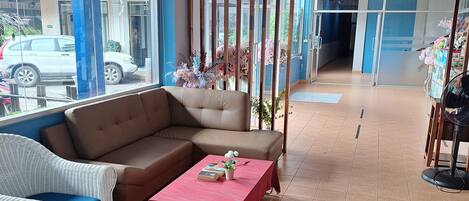 A spacious lobby with a brown sofa, white wicker chairs, and a red table with books and a plant.