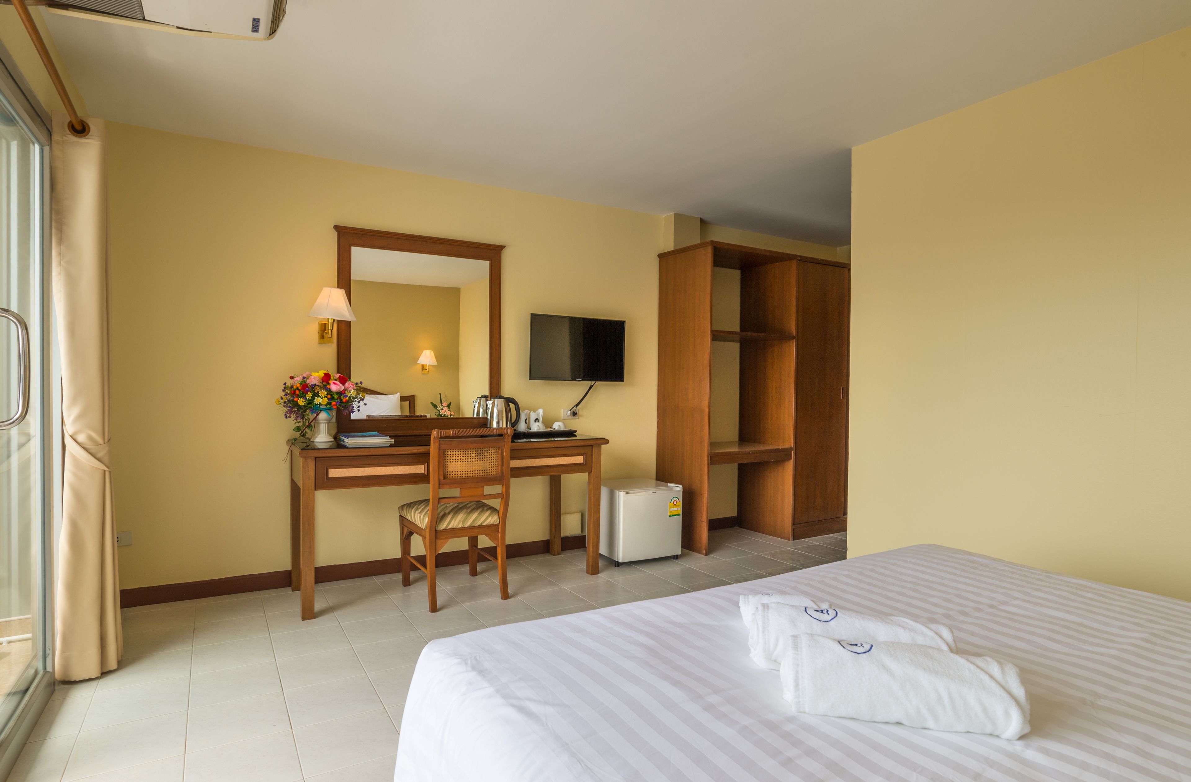 A hotel room with a bed, a desk with a chair, a television, a small refrigerator, and a wardrobe.
