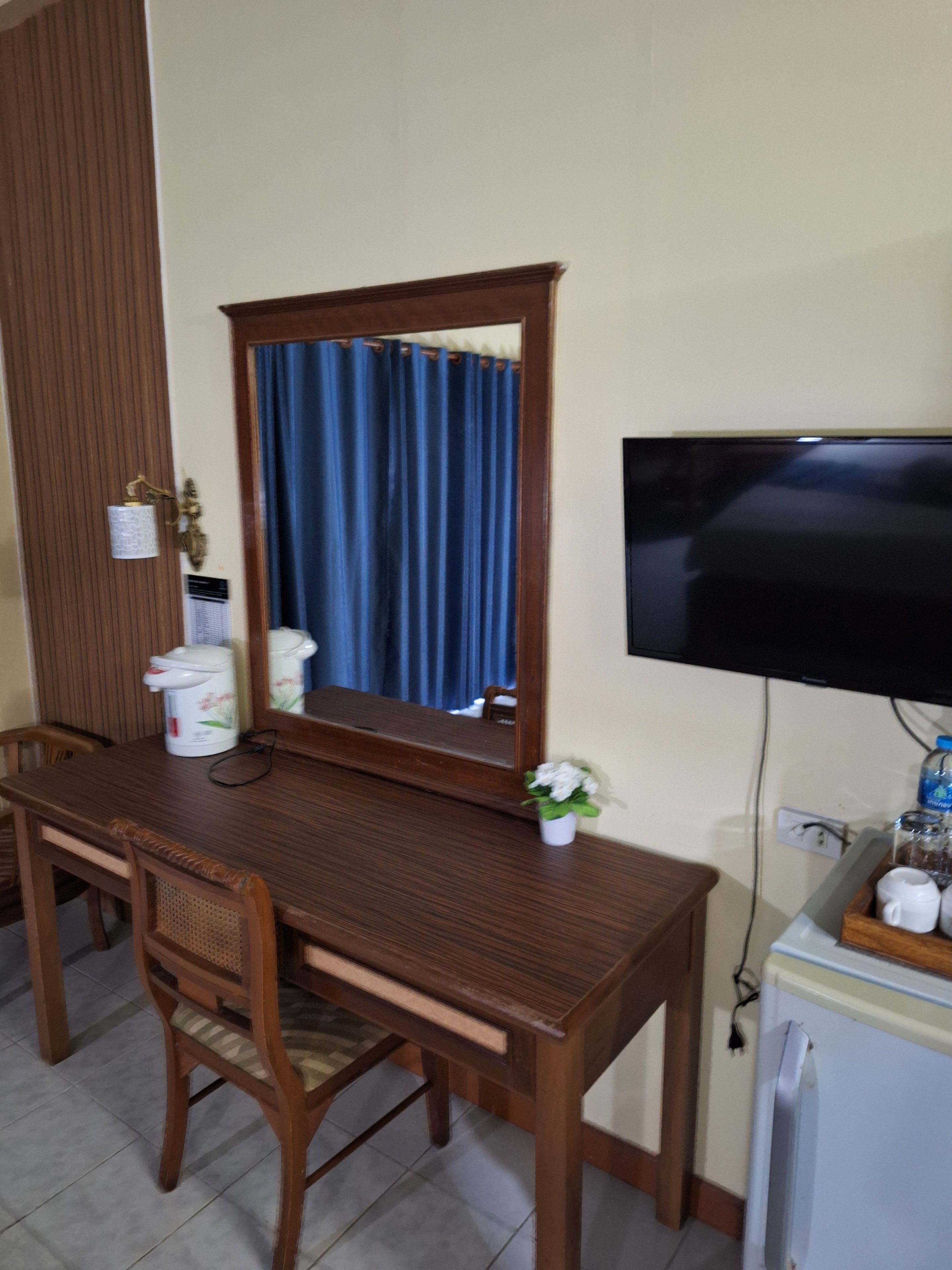 Une pièce avec un bureau en bois, une télévision, un miroir et une petite plante.