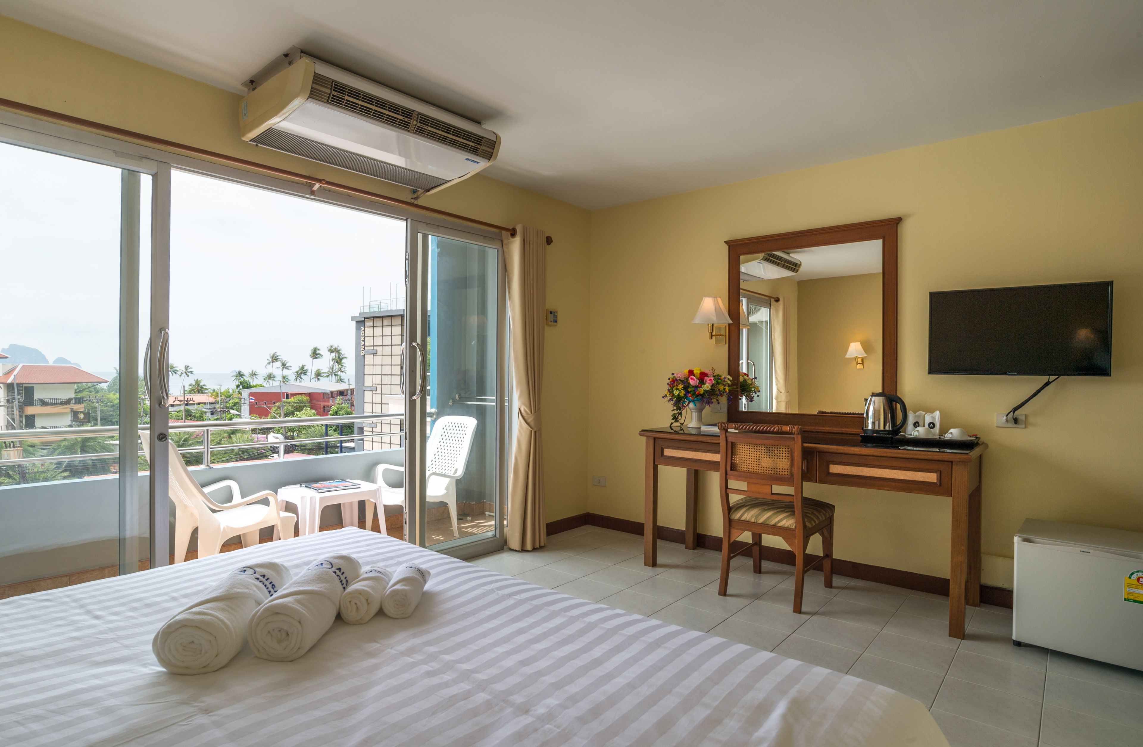 Une chambre d’hôtel comprenant un lit, un bureau, une chaise, une télévision et un balcon avec des chaises.