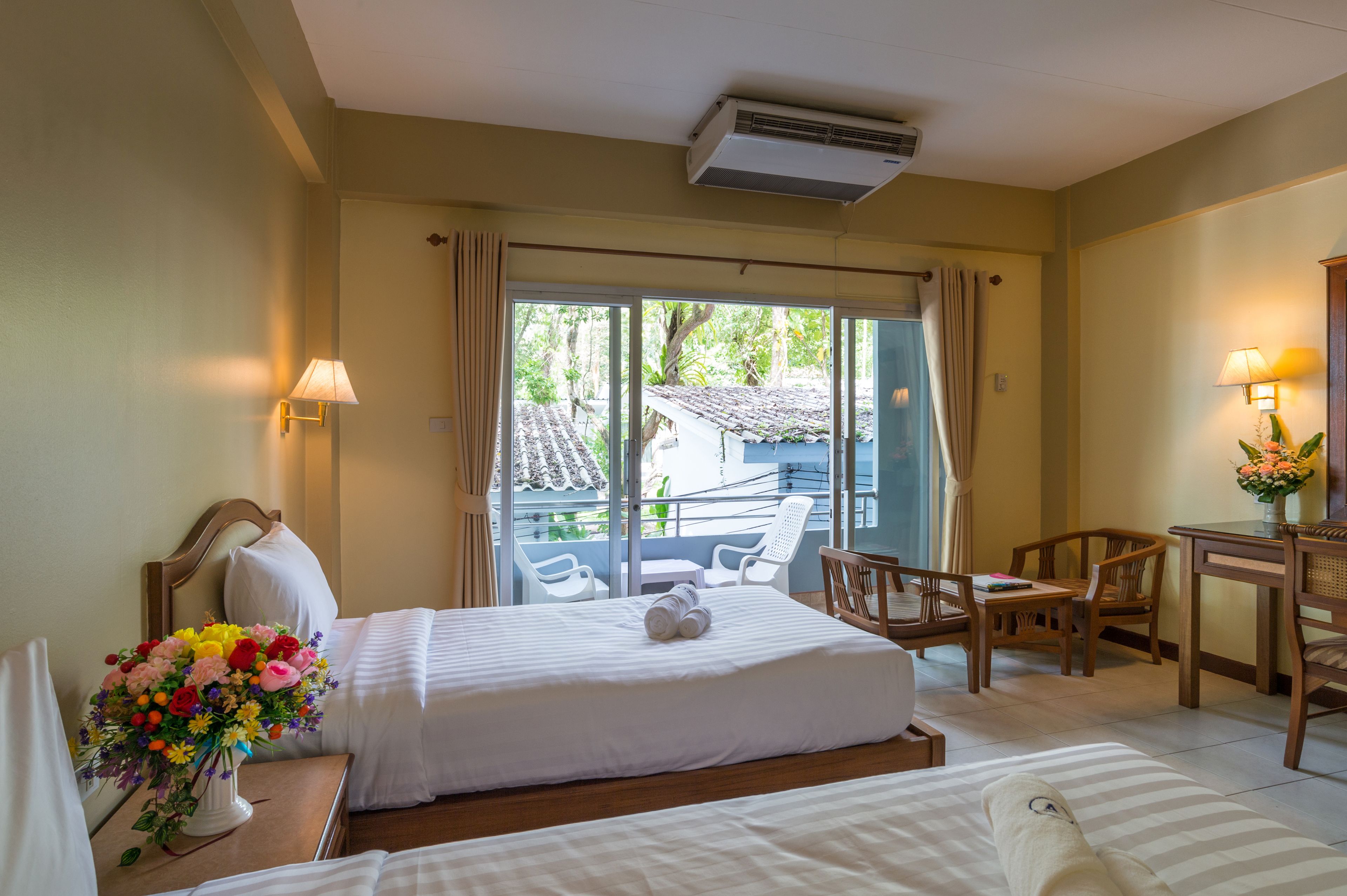 A hotel room with a bed, a desk, a chair, a lamp, and a view of the outdoors.