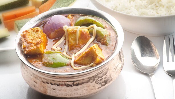 Un bol de curry aux légumes et au tofu, accompagné d’un bol de riz blanc et d’une assiette de légumes coupés en tranches.