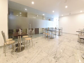 Un amplio comedor con suelo de mármol y muebles modernos, incluyendo mesas y sillas.