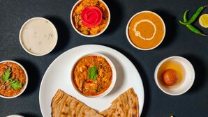 Verschiedene indische Gerichte, darunter Curry, Naan-Brot und ein Dessert.