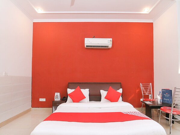 A hotel room with a large bed, red walls, a white ceiling, and a small table with a chair.