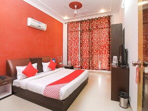 Een hotelkamer met een bed, een bureau, een stoel, een airconditioning, een televisie en een deur.