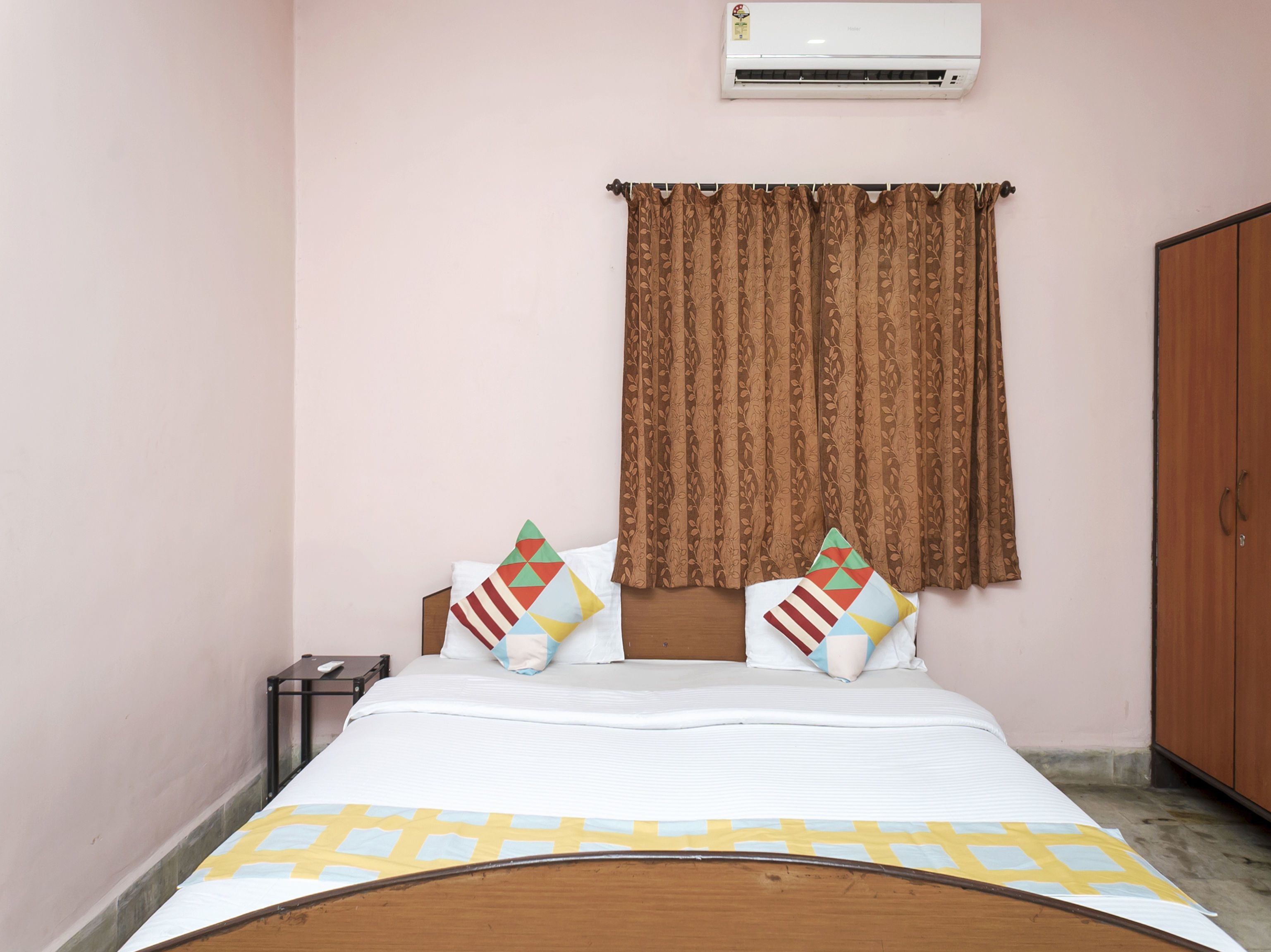 A bedroom with a bed, pillows, a nightstand, an air conditioner, and a wardrobe.