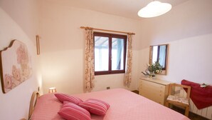 A bedroom with a bed, a dresser, a chair, a window with curtains, and a mirror on the wall. - Appartamenti Il Sogno (Capoliveri)
