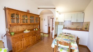 A kitchen with wooden cabinets, a dining table with chairs, and a small island with a sink. - Appartamenti Il Sogno (Capoliveri)
