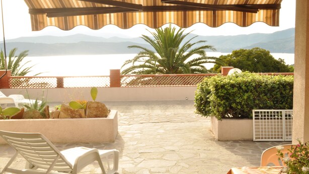 An outdoor patio with a view of the sea, stone flooring, and potted plants. - Appartamenti Il Sogno (Capoliveri)