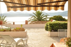 An outdoor patio with a view of the sea, stone flooring, and potted plants. - Appartamenti Il Sogno (Capoliveri)