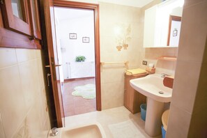 Baño con lavamanos, inodoro y ducha. Hay un perchero y una planta pequeña en la pared.