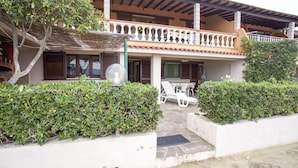 A two-story building with a balcony, white walls, and a tiled roof. There are potted plants and outdoor furniture. - Appartamenti Il Sogno (Capoliveri)