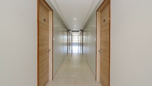 Un long couloir étroit, avec des portes en bois de chaque côté et un sol carrelé.