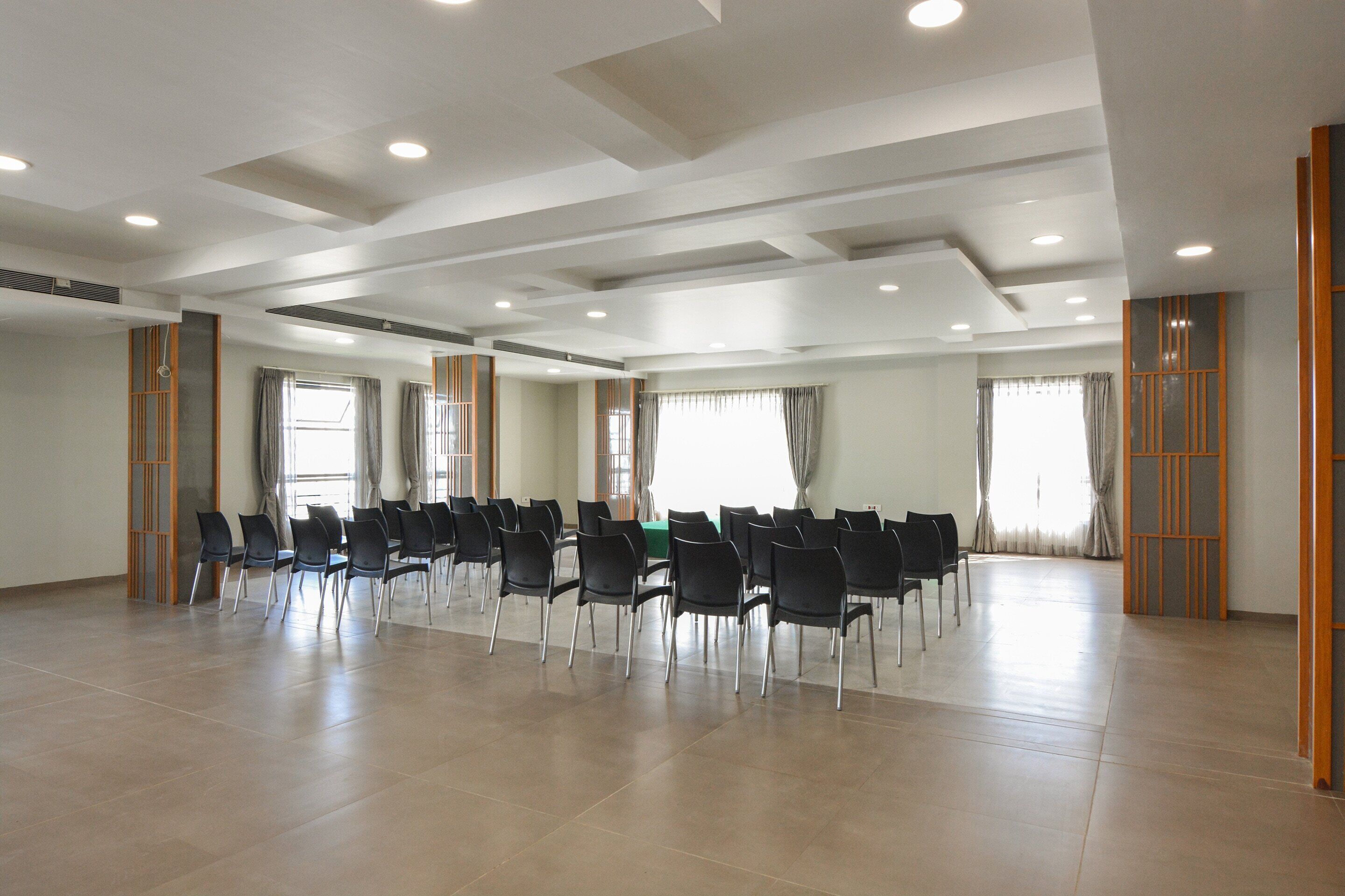 A spacious conference room with rows of chairs, large windows with curtains, and a modern ceiling design.