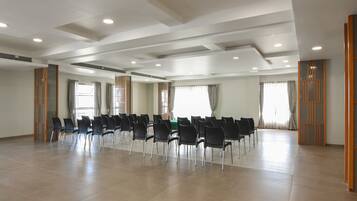 A spacious conference room with rows of chairs, large windows with curtains, and a modern ceiling design.
