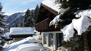 Un chalet en bois doté d’un balcon, entouré d’arbres et de montagnes couverts de neige.